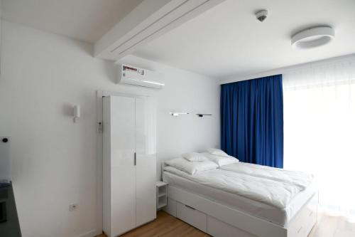 a white bedroom with a bed and a blue curtain at Blue Sky Apartments Rezydencja Niechorze - 302 in Niechorze