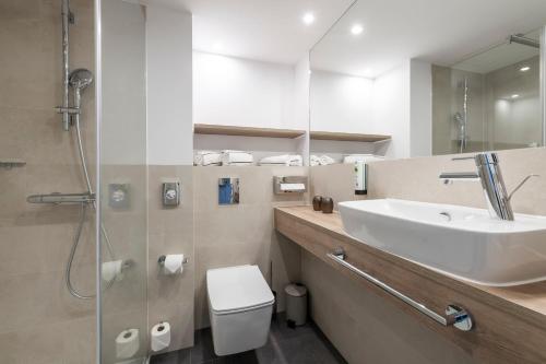 ein Badezimmer mit einem Waschbecken, einem WC und einem Spiegel in der Unterkunft HARBR. Hotel Ludwigsburg in Ludwigsburg