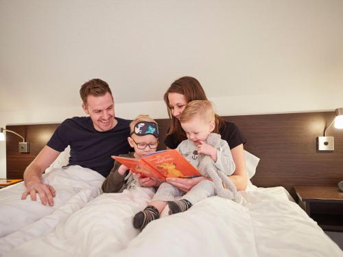 a family sitting on a bed reading a book at Villa Buitenhof De Leistert 15 in Roggel