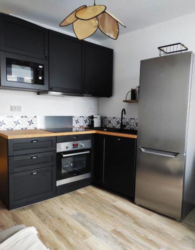 une cuisine avec des armoires noires et un réfrigérateur en acier inoxydable dans l'établissement L'escapade, à La Bourboule