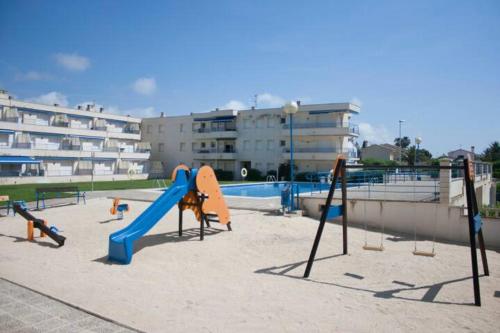 um parque infantil com um escorrega na areia em frente a um edifício em Apartamento Eucaliptus B - Delta del Ebro em L'Eucaliptus