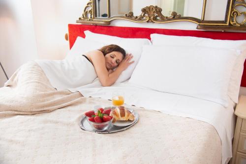 a woman laying in bed with a tray of food at Villa Bina Sea Hotel in Ischia