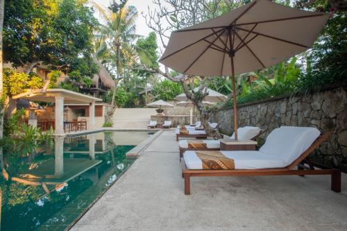 a row of lounge chairs and an umbrella next to a pool at Komaneka at Monkey Forest Ubud in Ubud