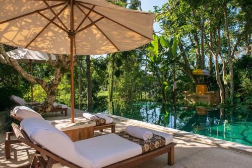 a patio with chairs and an umbrella and a pool at Komaneka at Monkey Forest Ubud in Ubud