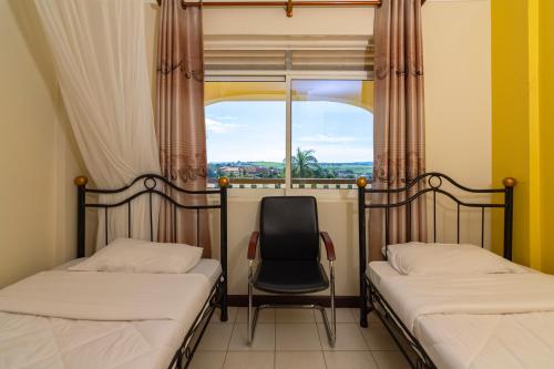 two beds and a chair in a room with a window at Karibu BB Suites in Entebbe