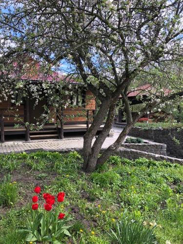 a tree and red flowers in front of a building at Будинок для відпочинку в лісі in Berëzovka