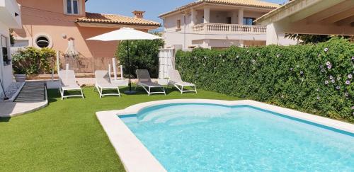 einen Pool in einem Garten mit Stühlen und einem Sonnenschirm in der Unterkunft VILLA BERNA in Alcúdia
