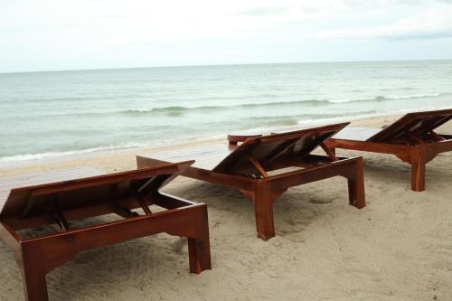 two wooden benches sitting on the beach near the ocean at Mumsa Beach Resort & Restaurant in Ban Huai Yang
