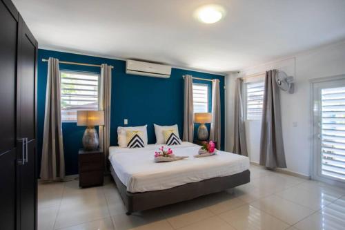 a bedroom with a large bed with blue walls and windows at Villa Curazon met privézwembad vlakbij het strand! in Jan Thiel
