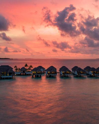 a group of overwater bungalows on the water at sunset at Finolhu, A Seaside Collection Resort, a Member of Design Hotels in Baa Atoll