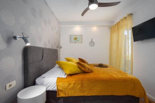 Villa Nava في Žrnovnica: غرفة نوم مع سرير مع وسائد صفراء ومروحة سقف