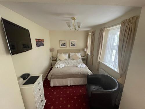 a bedroom with a bed and a chair and a television at The Southbourne Villa in Torquay
