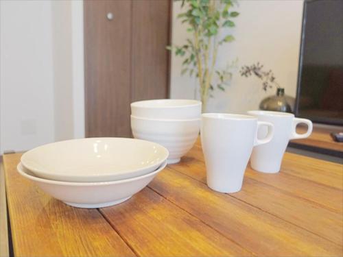 four white bowls and cups sitting on a wooden table at Apartment Hotel KANSO in Kyoto