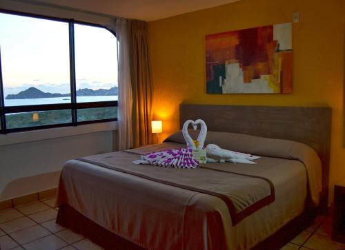 1 dormitorio con cama y ventana grande en Sunrock Hotel & Suites, en Cabo San Lucas