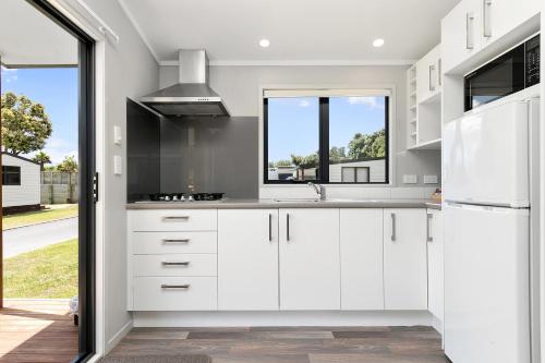 a kitchen with white cabinets and a window at Bowentown Beach Holiday Park in Waihi Beach