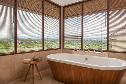 - une salle de bains avec une grande baignoire en face des fenêtres dans l'établissement Komaneka at Keramas Beach, à Keramas