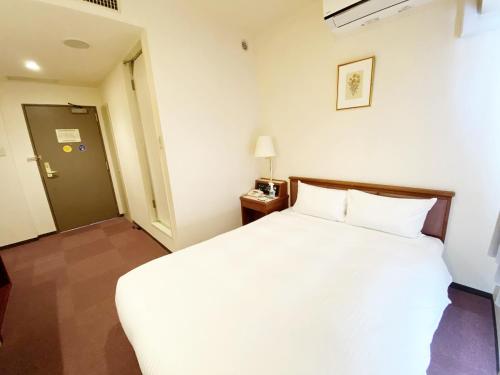 a hotel room with a white bed and a door at Smile Hotel Kitaasaka in Asaka