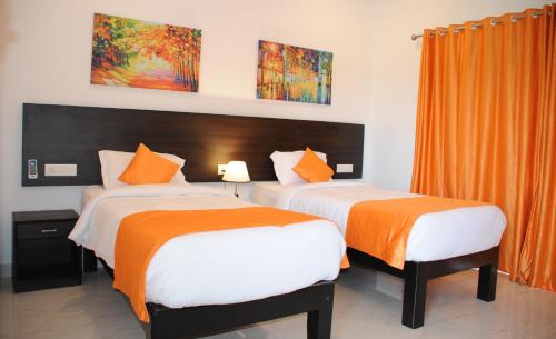two beds in a hotel room with orange curtains at JW HERITAGE in Anjuna