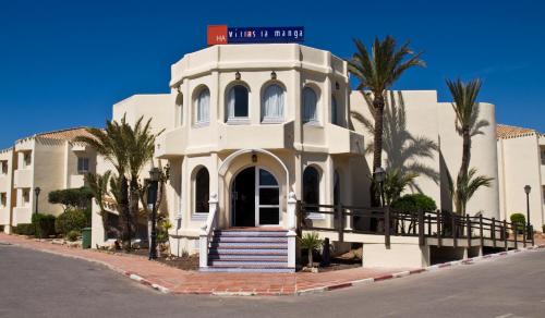 a white building with palm trees in front of it at Aparthotel Villas La Manga in La Manga del Mar Menor