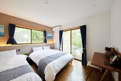 a bedroom with two beds and a desk and windows at 湖の辺の宿時翠 in Yamanakako