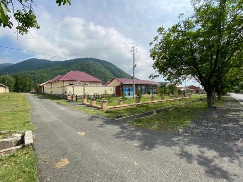 a road with a house and a tree and mountains at Alp Hotel in Qax