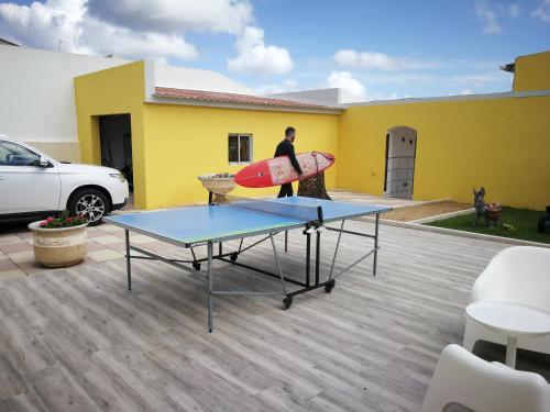 a man holding a surfboard on a table in front of a house at Surf House Helena in Baleal