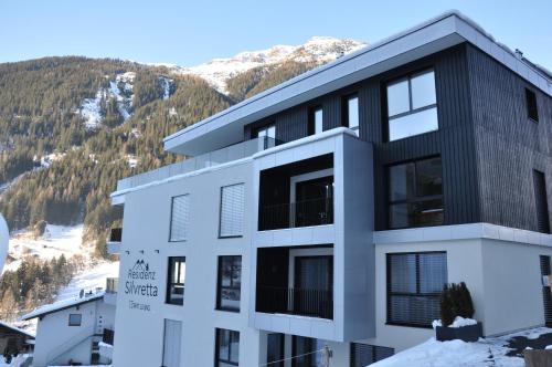 a white and black building with mountains in the background at Das luxuriöse alpine Apartment in der Residenz Silvretta - Inklusive Silvretta Card Premium in See