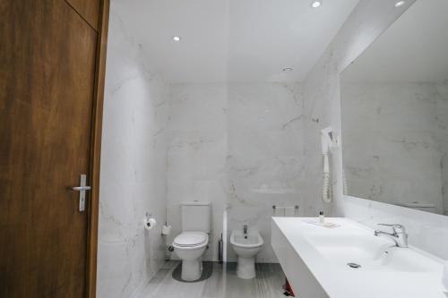 a white bathroom with a toilet and a sink at Hotel Premium Porto Maia in Maia