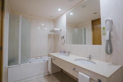 a bathroom with two sinks and a tub and a mirror at Hotel Premium Porto Maia in Maia