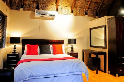 a bedroom with a large bed with red and orange pillows at Impa-Lala Country Estate in Bloemfontein