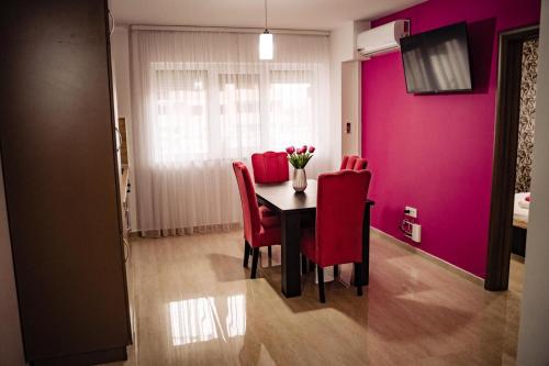 ein Esszimmer mit rosa Wänden und einem Tisch mit roten Stühlen in der Unterkunft Apartment Gabriela's Home in Oradea