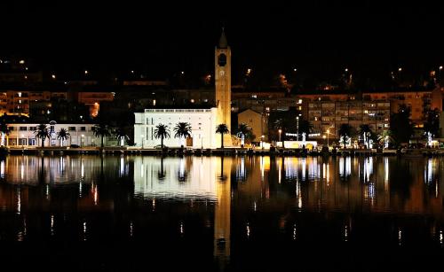 a city at night with a clock tower and a body of water at Apartments Neda in Ploče