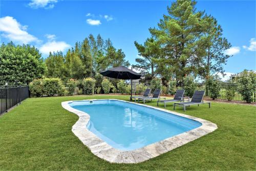 a swimming pool in a yard with two chairs and an umbrella at Mountainview Escape Rothbury 5br house in Rothbury