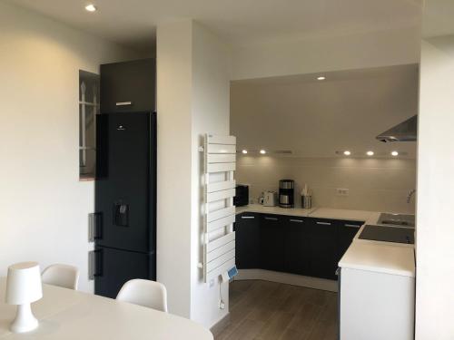 a kitchen with a black refrigerator and white cabinets at "Aux Balcons du Riou" avec vue mer 180 degrés in Vence