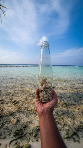 a hand holding a bottle filled with rocks in the ocean at New Breeze Thoddoo Inn in Thoddoo