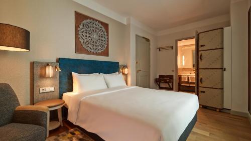 a hotel room with a large white bed and a chair at voco The Hague by IHG in The Hague