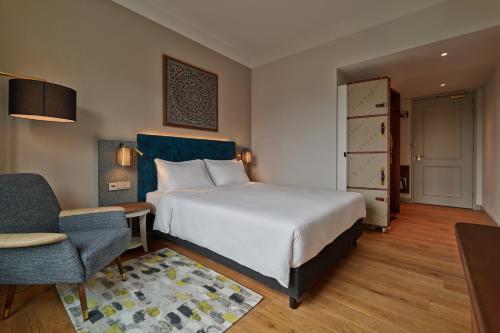a bedroom with a large white bed and a chair at voco The Hague by IHG in The Hague