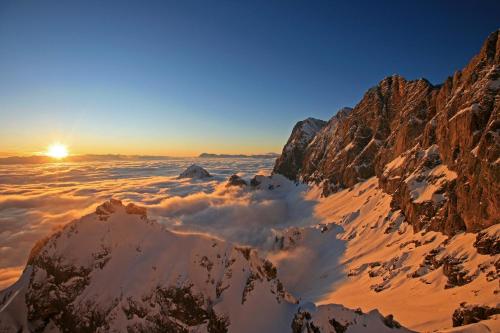 a view from the summit of a mountain with the sun rising over the clouds at Adlernest in Ramsau am Dachstein