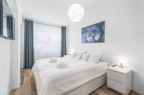 a white bedroom with a large white bed and a window at Seaside Breeze Stylish Apartment Balcony & Parking by Renters in Międzyzdroje