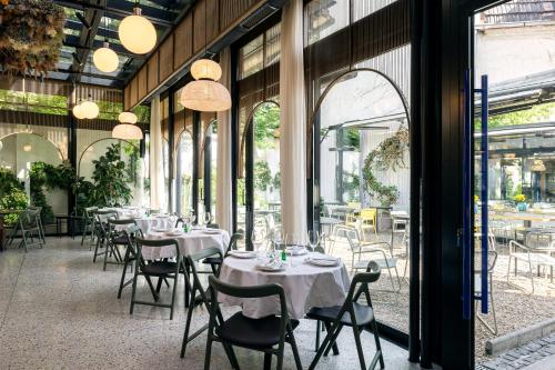 un ristorante con tavoli e sedie bianchi e finestre di Pavilion Hotel & Social Club a Belgrado