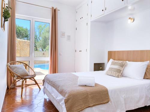 a bedroom with a bed and a chair and a window at REFÚGIO DO CARANGUEJO - Praia da Luz - WiFi, Private Pool & BBQ in Luz
