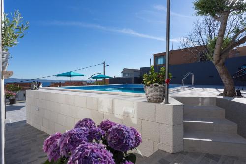 a retaining wall with purple flowers next to a swimming pool at Apartments Lidija - sea view apartment with exclusive right of using hot tub or split level apartment with exclusive right of using pool in Podstrana