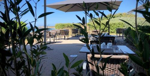 a patio with tables and chairs and an umbrella at Logis Hôtel & Restaurant LES MOUETTES - Larmor Plage, Proche de LORIENT in Larmor-Plage