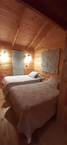 two beds in a wooden room with two windows at Cabaña las trancas in Nevados de Chillan