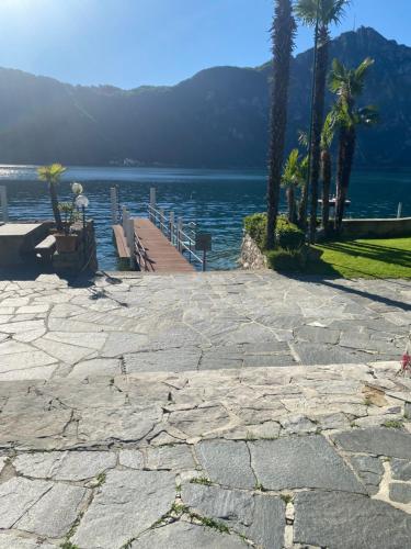 a stone walkway next to a lake with palm trees at Holiday on the Lake Lugano in Bissone
