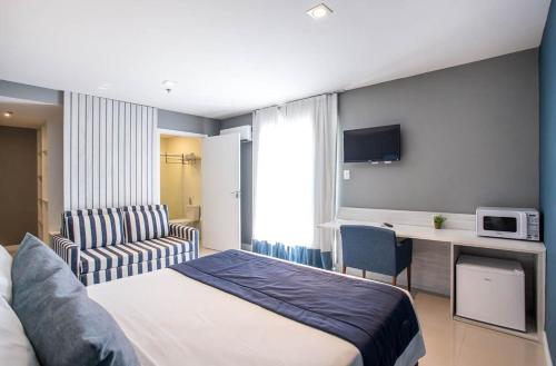 a hotel room with a bed and a desk with a microwave at Flat 402 in Cabo Frio 700m from the beach in Cabo Frio