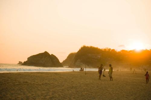 Eine Gruppe von Menschen steht bei Sonnenuntergang am Strand. in der Unterkunft Hotel Estrella de Mar in Zipolite