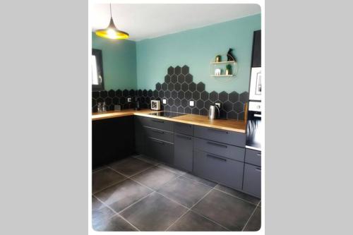 une cuisine avec des armoires noires et un mur bleu dans l'établissement Charmante Maison La Source, à Grandes Sables