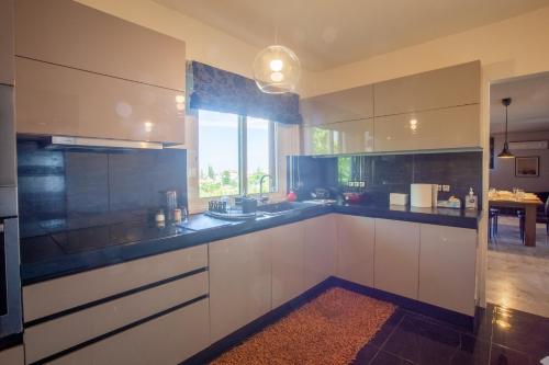 a kitchen with white cabinets and a large window at Τraditional fully detached villa on a luxurious hillock of Thessaloniki with its own garden also for family & wedding gatherings for 10 to 25 people only 15 minutes from airport in Thessaloniki