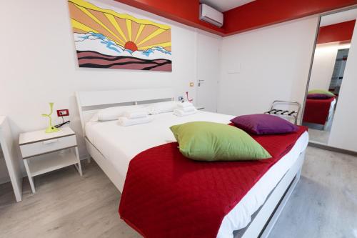 a bedroom with a white bed with a red blanket and colorful pillows at Valmontone Travel Rooms in Valmontone
